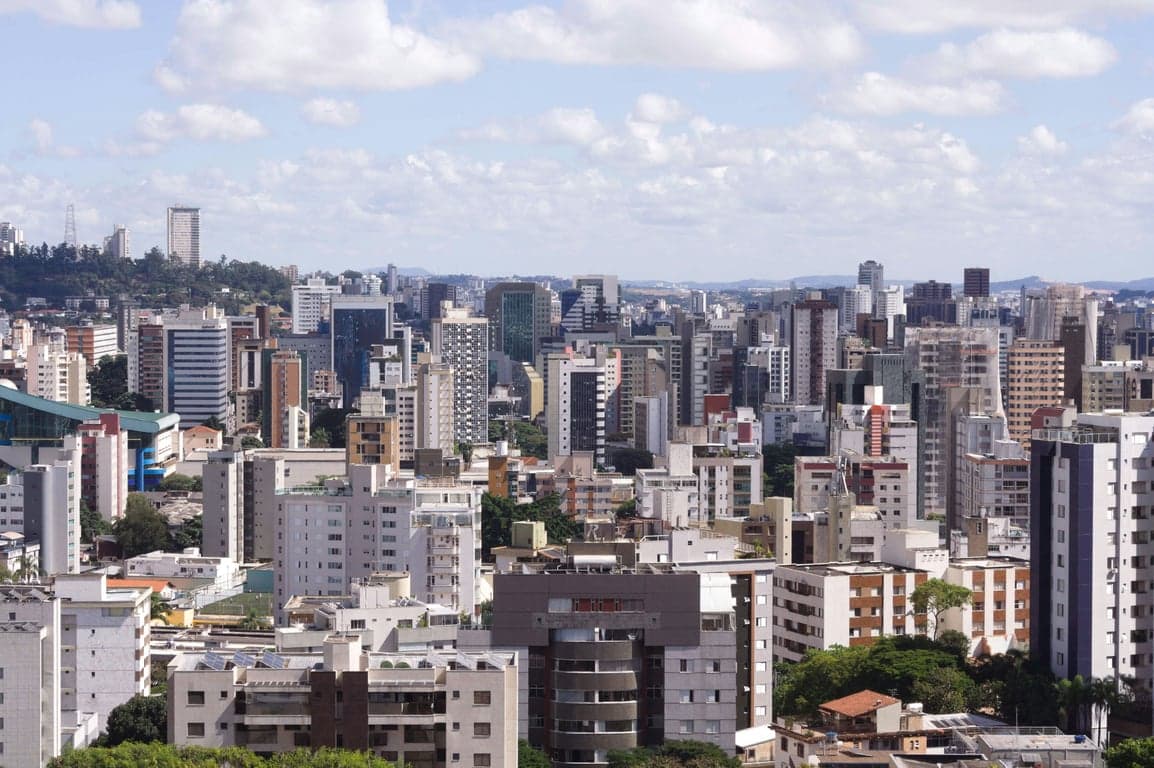 Rua arborizada de bairro residencial em Belo Horizonte com prédios baixos e calçada ampla em primeiro plano